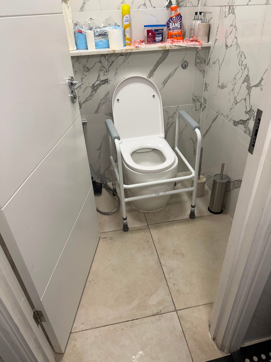 The same cubicle after the project, with a height-adjustable toilet support frame fitted around the toilet