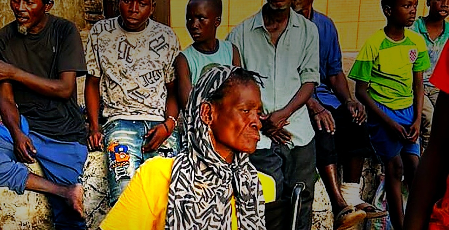 An elderly woman in a wheelchair surrounded by community members at a distribution